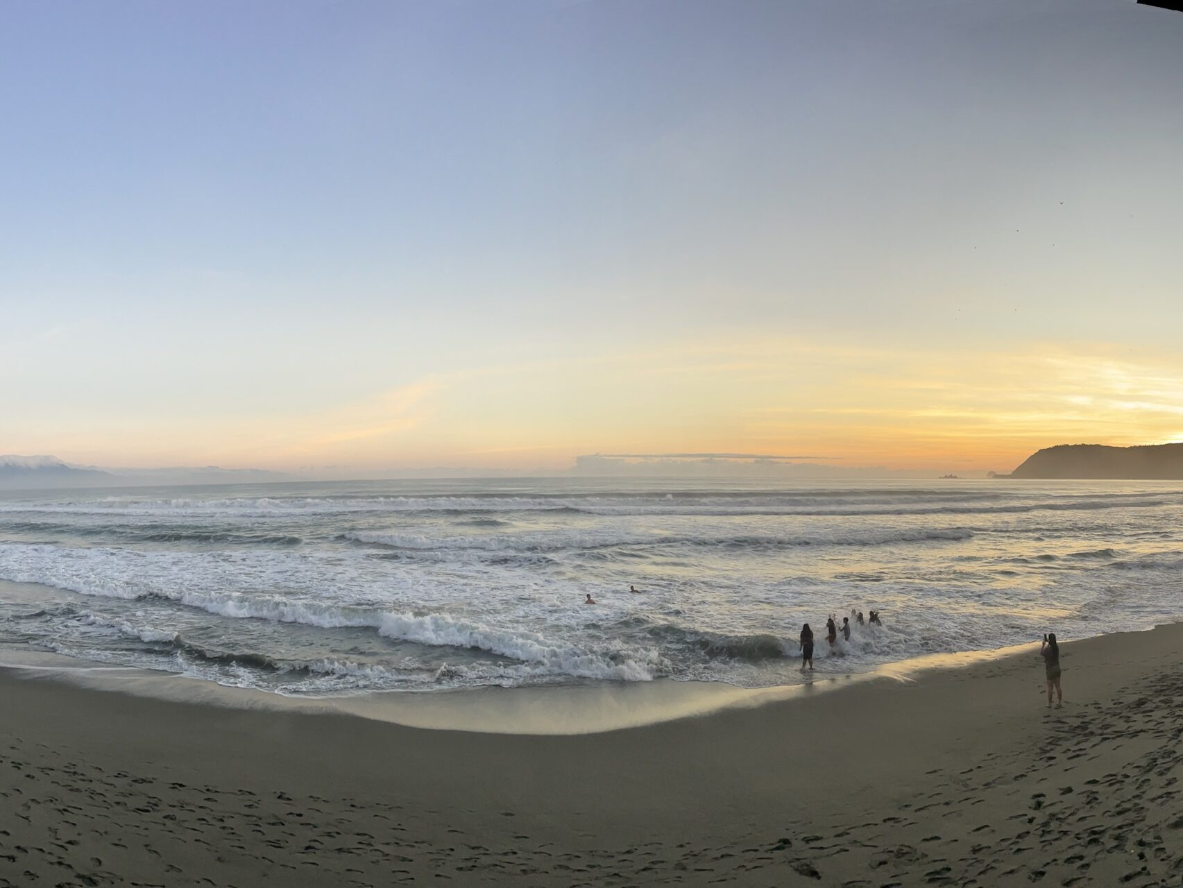 A panoramic view of a sandy beach at sunset, with gentle waves lapping at the shore and people enjoying the shoreline.